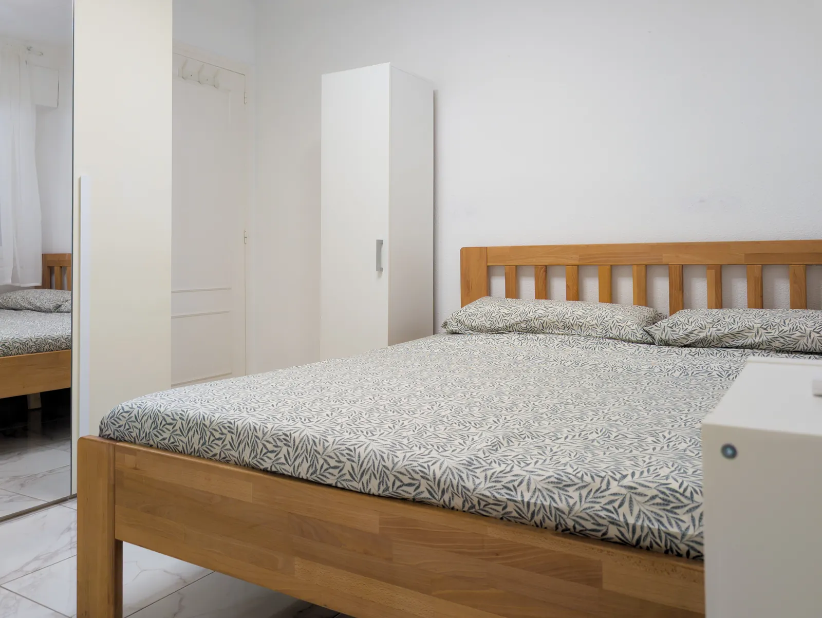 Double bed with a wooden headboard and patterned linen, a wardrobe beside it