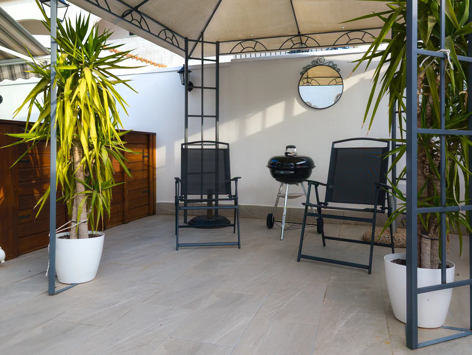 Gazebo with two folding chairs, a kettle barbecue and potted palms