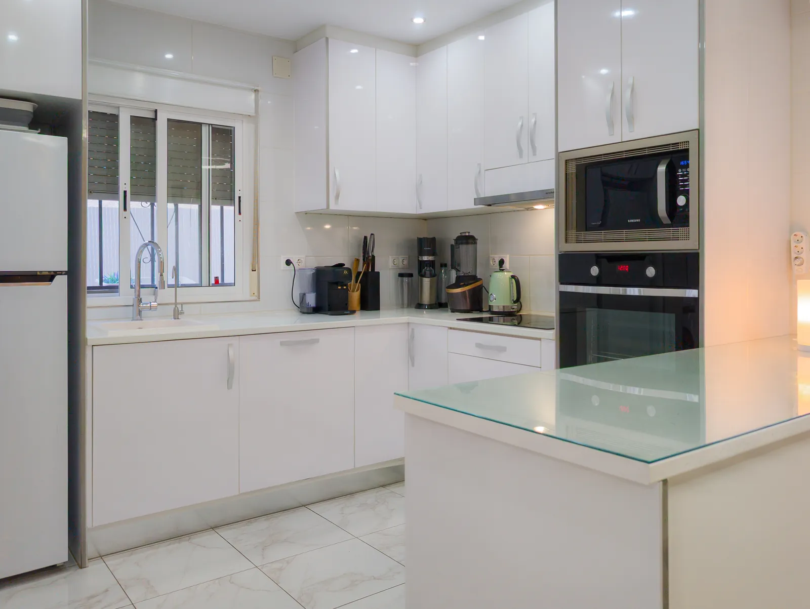 White kitchen with oven, microwave, hob, coffee machine, kettle and a glass-topped breakfast bar